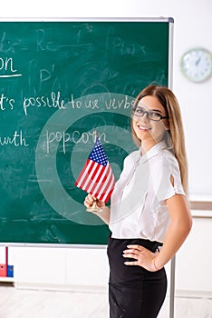 The young female english language teacher standing in front of the blackboard