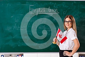 The young female english language teacher standing in front of the blackboard