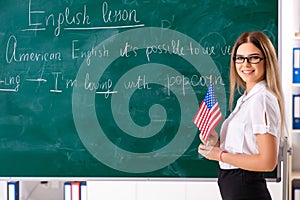 The young female english language teacher standing in front of the blackboard