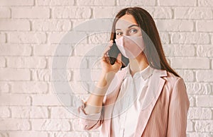 Young female entrepreneur in pink suit and protective face mask talk smart phone