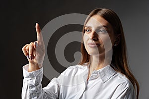 Young female entrepreneur touching virtual screen against grey studio background