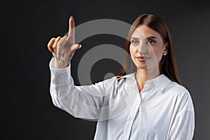 Young female entrepreneur touching virtual screen against grey studio background