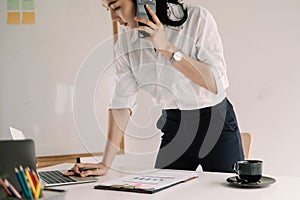 Young female entrepreneur working laptop computer and talking mobile phone to client