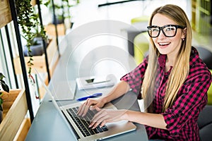 Young female entrepreneur working sitting at a desk typing on her laptop computer in a office, view from above