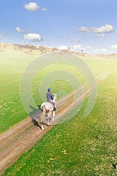 Young female equestrian riding horse along rural countryside. Rider on horseback going through green hillside.Travelling along.