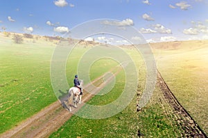 Young female equestrian riding horse along rural countryside. Rider on horseback going through green hillside.Travelling along.