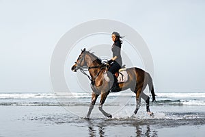 young female equestrian riding horse with ocean