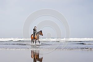 young female equestrian riding horse on sandy