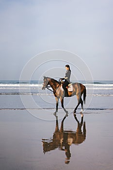 young female equestrian riding horse on sandy beach