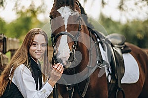 A young female equestrian stands near her horse and prepares for a competition.