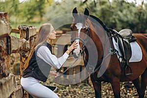 A young female equestrian stands near her horse and prepares for a competition.