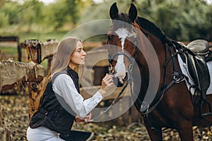 A young female equestrian stands near her horse and prepares for a competition.