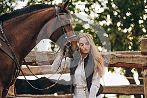 A young female equestrian stands near her horse and prepares for a competition.