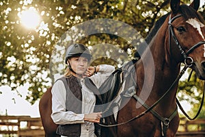 A young female equestrian stands near her horse and prepares for a competition.