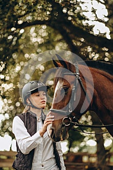 A young female equestrian stands near her horse and prepares for a competition.