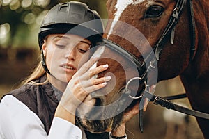 A young female equestrian stands near her horse and prepares for a competition.