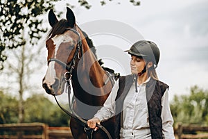 A young female equestrian stands near her horse and prepares for a competition.