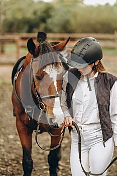 A young female equestrian stands near her horse and prepares for a competition.