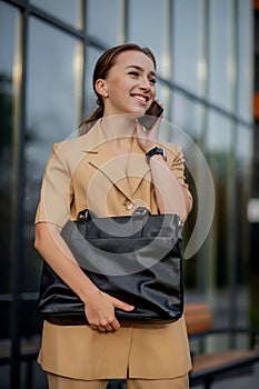 Young female executive standing outside office building talking on cell phone. Caucacian businesswoman making a phone call while