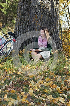 Young female with fall autumn leaves and red book in the hands in vintage old style clothes outdoors in the park