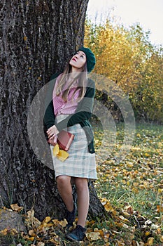 Young female with fall autumn leaves and red book in the hands in vintage old style clothes outdoors in the park