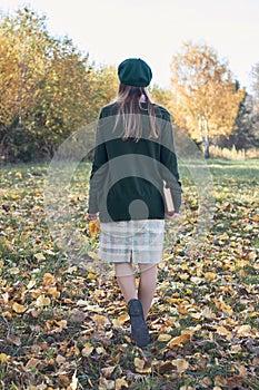 Young female with fall autumn leaves and red book in the hands in vintage old style clothes walking outdoors in the park