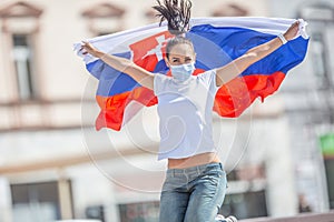 Young female fan of Slovakia jumps from joy on a street holding a flag