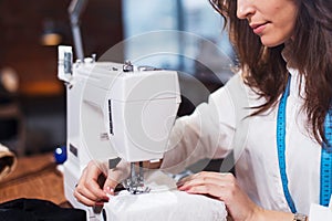 Young female fashion designer working on sewing machine in a workshop