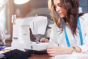 Young female fashion designer working on sewing machine in a workshop