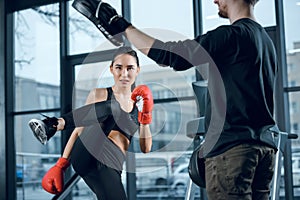 young female fighter performing low kick with trainer