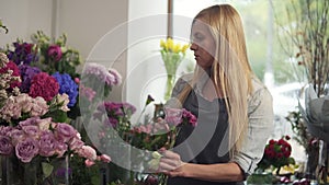 Young female florist business owner working and preparing flower arrangements in her shop, with fresh flowers. She is