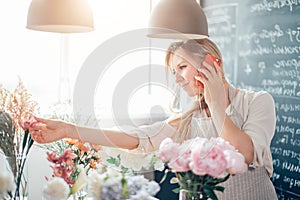 Young female florist talking on phone and making notes at flower shop.