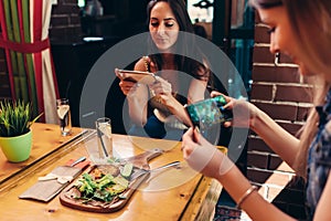 Young female food bloggers photographing their lunch with smartphones in restaurant