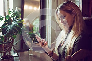 Young female freelancer chatting on mobile phone while sitting on the couch in vintage cafe