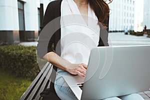 Young female freelancer making labor market research on modern laptop, sits on outdoors in urban street