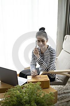 Female freelancer receive order on smart phone and writing address on cardboard box.
