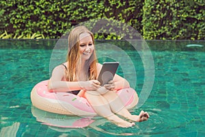 Young female freelancer sitting near the pool with her laptop in the hotel browsing in her smartphone. Busy at holidays