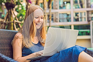 Young female freelancer sitting near the pool with her laptop in the hotel browsing in her smartphone. Busy at holidays