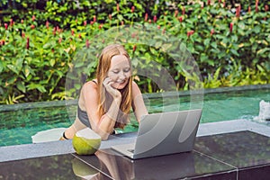 Young female freelancer sitting near the pool with her laptop in the hotel browsing in her smartphone. Busy at holidays