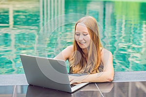 Young female freelancer sitting near the pool with her laptop in the hotel browsing in her smartphone. Busy at holidays