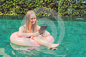 Young female freelancer sitting near the pool with her laptop in the hotel browsing in her smartphone. Busy at holidays