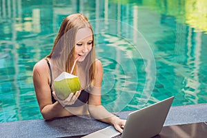 Young female freelancer sitting near the pool with her laptop in the hotel browsing in her smartphone. Busy at holidays. Distant w
