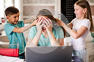 A young female freelancer works from home remotely using a laptop. Women children do her hair and interfere with work