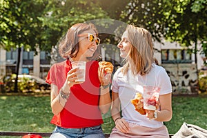 Young female friends laugh and eat yoghurt outdoors