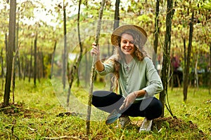 Young female gardener smiles on her farm sitting with garden trowel in soil among plants. Happy cauasian woman in her photo