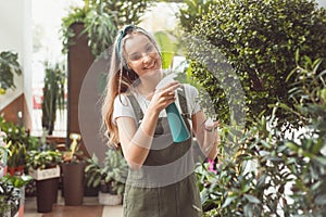 Young female gardener in spraying myrtle tree houseplant in flower store or greenhouse