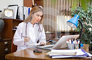 Young female general practitioner studies the patient's outpatient card, writing down the appointment