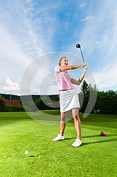 Young female golf player on course doing golf swing