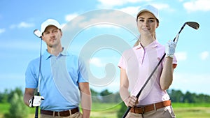 Young female golfer with partner holding clubs and smiling on camera, recreation