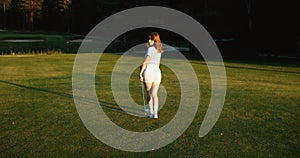 A young female golfer is walking along the golf course. Back view